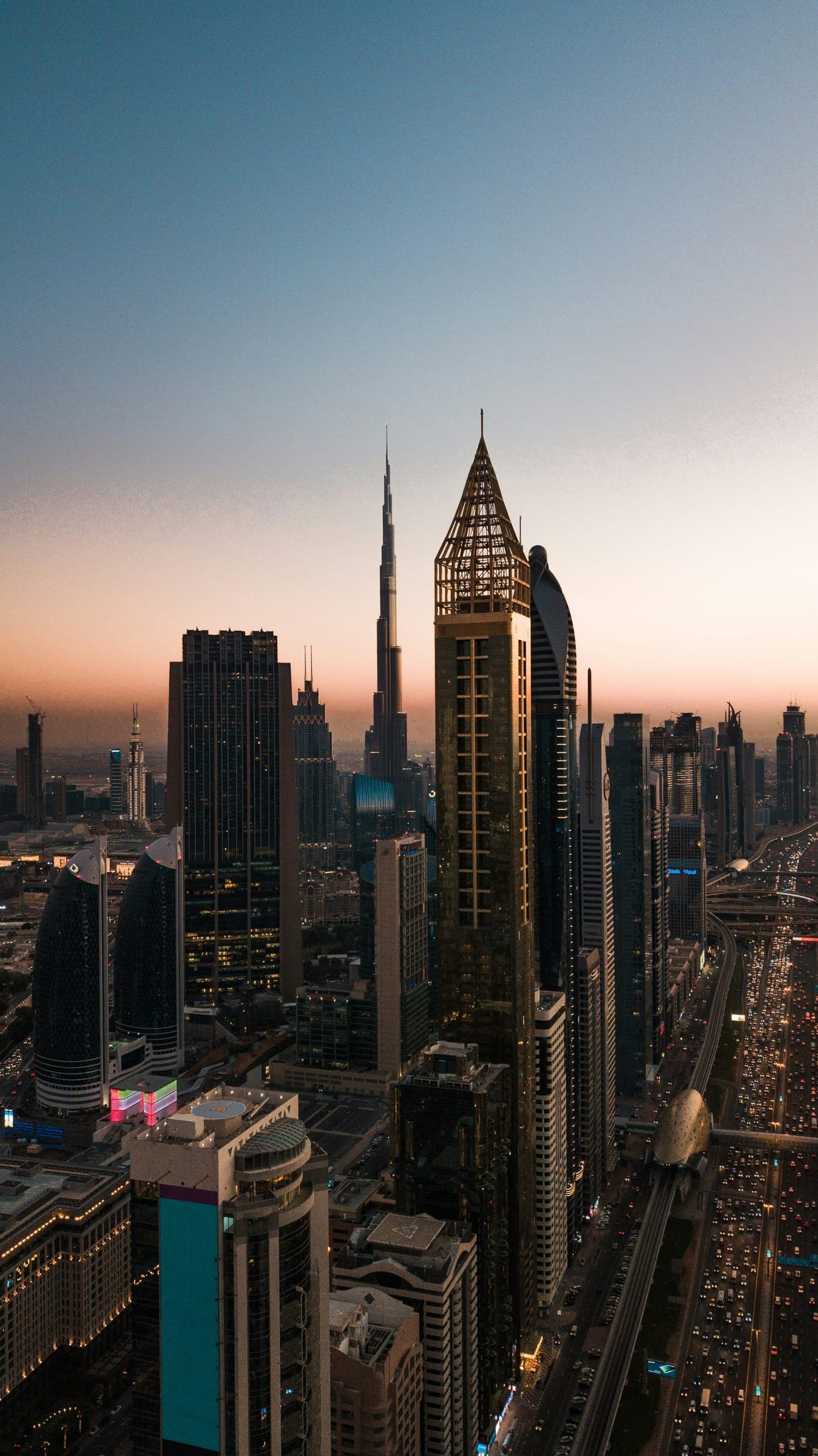 Towers lining Sheikh Zayed Road at dusk, with the Burj Khalifa on the skyline and traffic below.