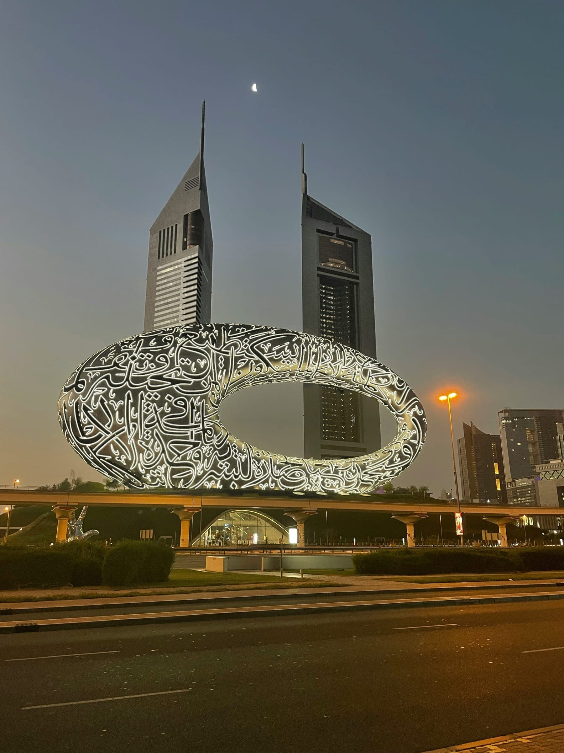 The Museum of the Future lit at dusk beside Sheikh Zayed Road, with the Emirates Towers behind.